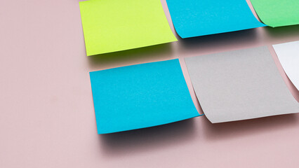 A collection of bright blue and green adhesive notes shown from a side angle on a smooth pink background, ideal for creative concepts.