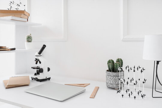 Laptop with microscope and molecular model on table in student's room - Powered by Adobe