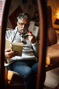 Man reads book while sitting in chair and smoking pipe