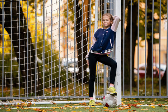 Girl standing with foot on soccer ball near goal post on field.