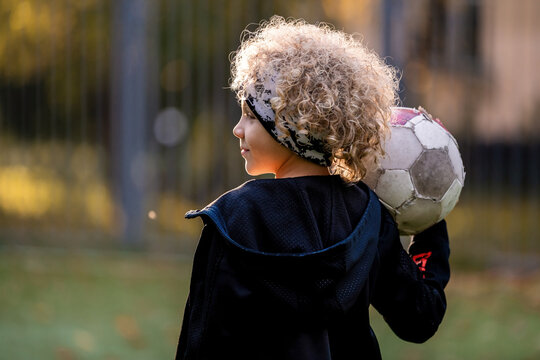 kid with curly hair holding a soccer ball on shoulder on field