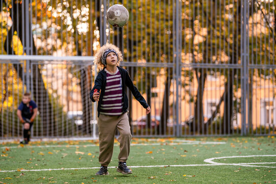 boy with curly hair trains with a soccer ball at an outdoor stadium.