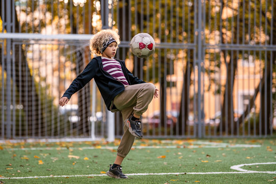 boy with curly hair juggles a soccer ball on a green field