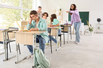 Fototapeta premium Bullied teenage boy sitting at desk and his classmates in classroom