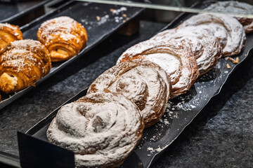 Close-up of sweet spiral pastries or ensaimadas dusted with powdered sugar arranged on a black tray...