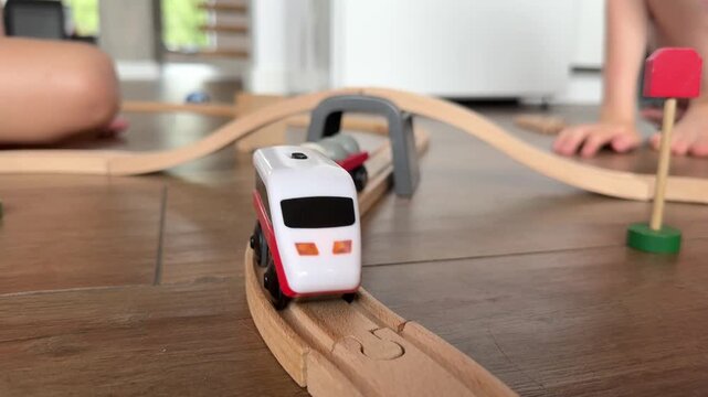 Toy train passing under wooden bridge on floor, child playing at home