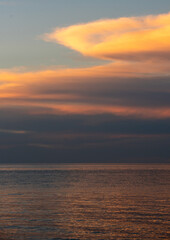Obraz premium Clouds gather above the ocean during sunset while the sky is painted with colors over the water in the early evening
