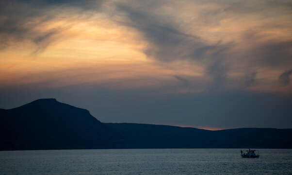 Sunset over water with a fishing boat near the coast and mountains in the distance, capturing the end of the day