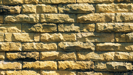 Rough yellow sandstone brick wall texture background, natural stone block surface for architectural exterior design.