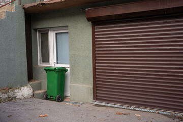 A green trash can in front of a house garage.

