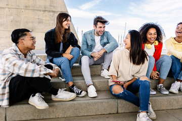 Multiracial group of young teenage student friends laughing together sitting outdoor. Youth community concept