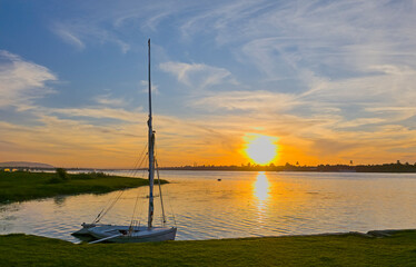 Traditional Egyptian felluca river sailing boat moored on the Nile riverbank with stunning evening sunset in background