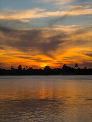 View across large wide river Nile in Egypt through rural countryside landscape with beautiful dramatic orange sunset and clouds in sky