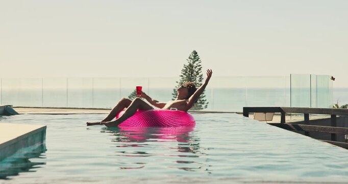 Float, drink and man in swimming pool at holiday home for relax in summer on vacation or weekend trip. Dancing, calm and person on inflatable with alcohol beverage in water for sunbathing at resort.