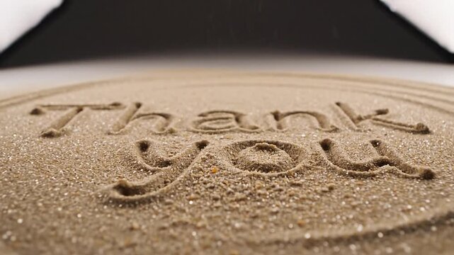 Sand falling, forming and revealing "Thank You" text etched into a textured surface