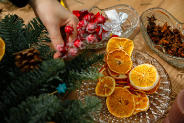 Close-up of a hand placing red frosty berries into a Christmas centerpiece next to a plate of dried orange slices and star anise.