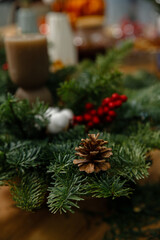 Vertical close-up of a pine cone nestled in fresh fir branches with red berries and cotton flowers, creating a festive Christmas decoration.