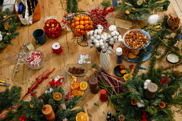 Festive Christmas centerpiece with a brown candle, fir branches, and dried orange slices on a wooden table. Cozy holiday atmosphere with a sparkling disco ball and citrus fruits in the background.