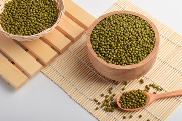 Mung beans in wooden bowls and spoon on bamboo mat background. Healthy organic legumes concept with green pulses, natural food ingredients.