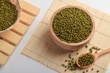 Mung beans in wooden bowls and spoon on bamboo mat background. Healthy organic legumes concept with...
