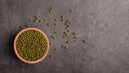 Raw mung beans in wooden bowl on dark stone background, flat lay with copy space.
