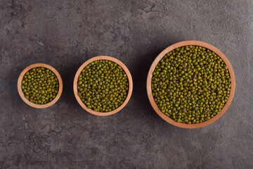 Green mung beans in wooden bowls flat lay isolated on dark stone background. Organic dried legumes...