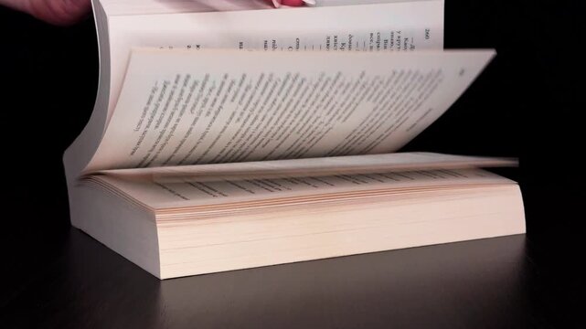 On a black background, a woman's hand opens a book with one hand. The pages turn by themselves and eventually smoothly overlap, creating an atmospheric minimalist frame
