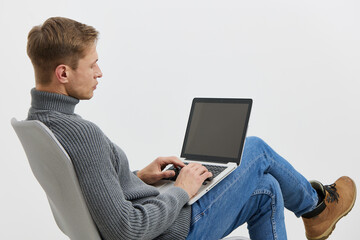 young caucasian man sitting use laptop work digital nomad casual sweater boots isolated on plain white background remote freelance concept
