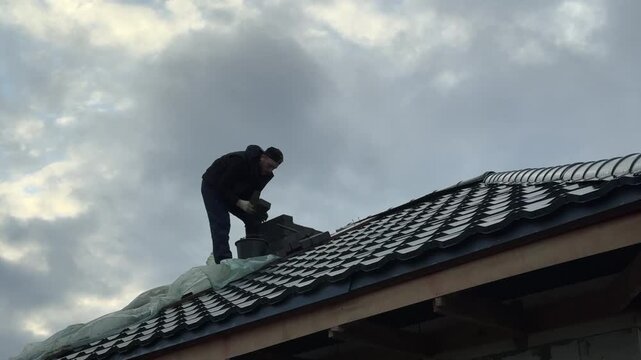 A master stove setter works on the roof of a house. He builds the masonry for a heating stove chimney.