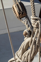 Nautical sailboat rigging detail with rope, wooden block, and coiled lines on a boat deck in sunlight