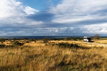 camper van parked in midst of golden autumn heath on the Swedish Island of Gotland with the Baltic Sea in the background