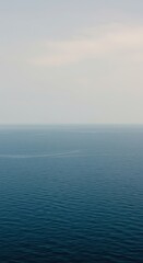 Fototapeta premium An immense, empty expanse of deep blue ocean water stretches endlessly toward a hazy horizon line under a pale and atmospheric, solitary sky ,endless ,freedom ,deserted