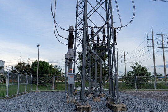 Ground level view of a high voltage transmission tower base and electrical equipment within a fenced substation area. Industrial infrastructure for electricity distribution and power grid management.