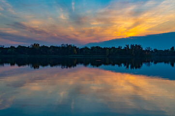Sunset over a calm lake, reflection and trees in the background in the early evening.