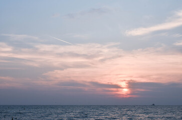 Fototapeta premium Pink, Cloudy sky at sunset; the trail of smoke from a jet aircraft is heading low to the right of the image.