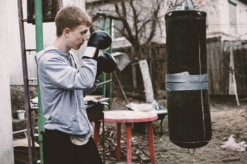 Young man in boxing gloves intensely training outdoors with a punching bag. A raw depiction of...