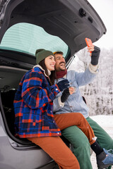 Couple using smart phone and drinking tea while taking winter vacation road trip break