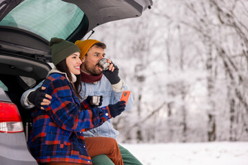 Couple using smart phone and drinking tea while taking winter vacation road trip break