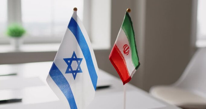 Diplomacy negotiation flags at meeting table talks. Close view shows Israeli and Iranian desk flags near empty chairs, implying delicate dialogue and formal protocol. Clear sign of peace talks.