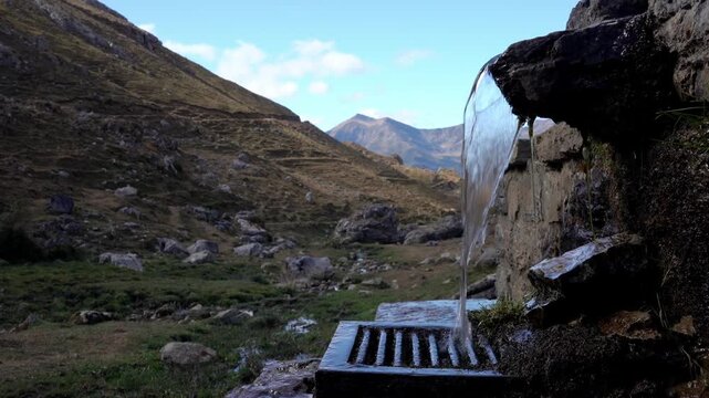 Crystal clear water running from a rustic stone fountain in a mountain valley. A refreshing spring flowing with a scenic landscape in the background