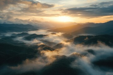 A breathtaking view of a mountain range, shrouded in a blanket of mist and clouds, as the sun rises over the horizon, casting a warm glow on the landscape.