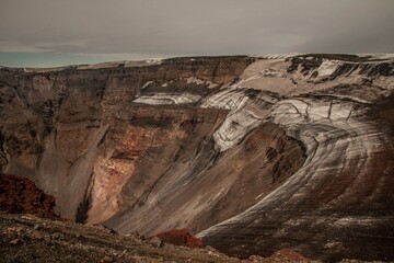 View from the edge of Plosky Tolbachik volcano crater, Kamchatka, with the inner crater slope partly covered in ice, creating a dramatic volcanic landscape.