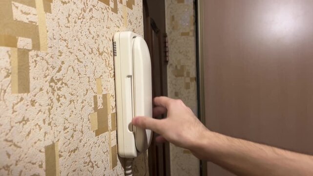 Hand hangs a white intercom on the intercom in the hallway near the front door