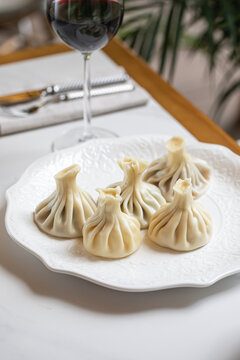 Traditional steamed khinkali dumplings with pleated dough served on a white plate in a bright interior
