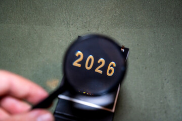 A magnifying glass is focusing on the number 2026, displayed prominently on a dark surface. This scene captures themes of perspectives and future planning in a creative context.