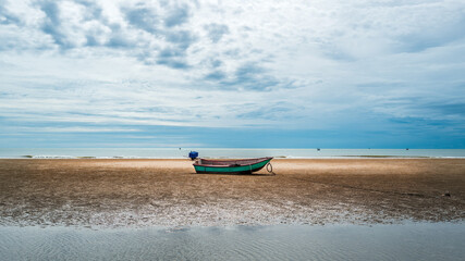Wooden fishing boat stuck on drought sand beach with cloudy sky.
