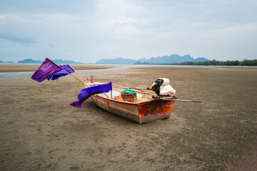 Wooden fishing boat with violet flags stuck on drought sand beach with cloudy sky.