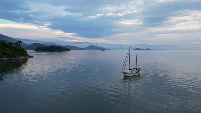 Paraty, Brazil: Aerial orbit drone footage of boat anchored in Paraty, an old town in state of Rio de Janeiro, Brazil during cloudy sunset with the Costa Verde coast in the background .