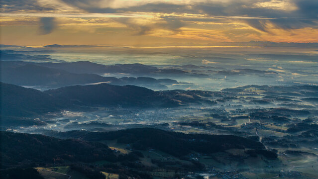 Blick auf das Tal bei Sonnenaufgang mit Nebel und den Ostalpen in der Ferne