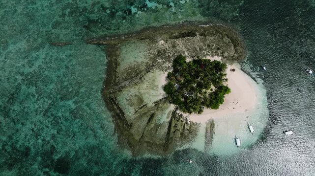 Top view of sandy island surrounded by reef and shallow turquoise sea with coconut trees. Guyam Island. Siargao, Philippines.
